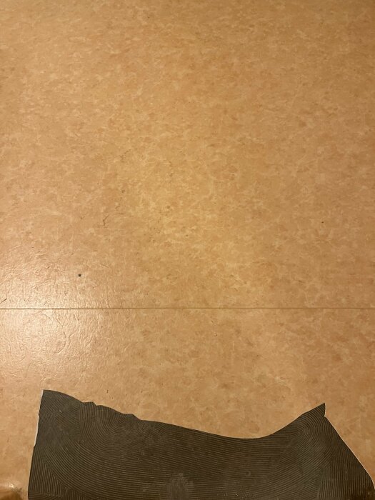Golv med beige mönster och del av en svart, böjd matta i nederkanten.