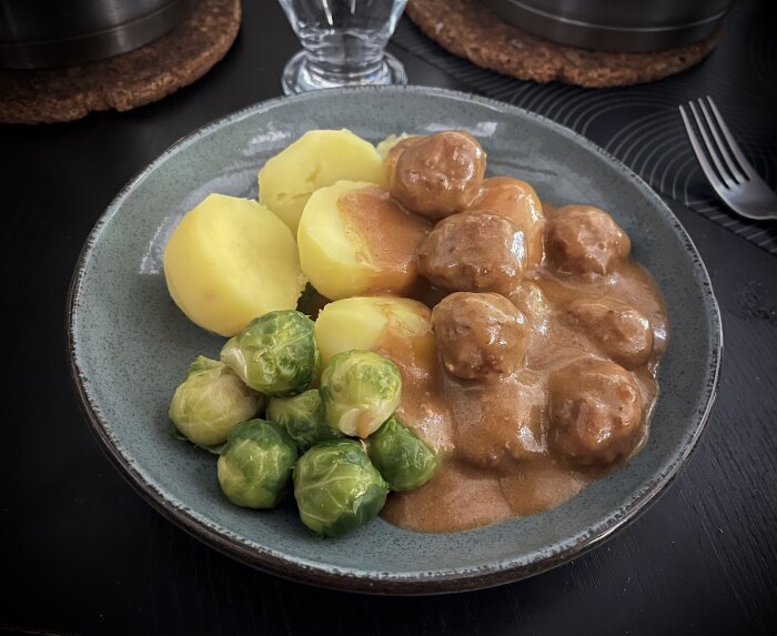 Tallrik med köttbullar i sås, kokt potatis och brysselkål.
