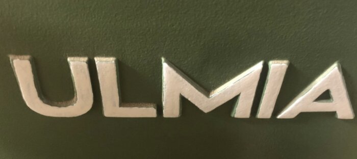 Närbild på logotypen "ULMIA" på en maskin med grön bakgrund.