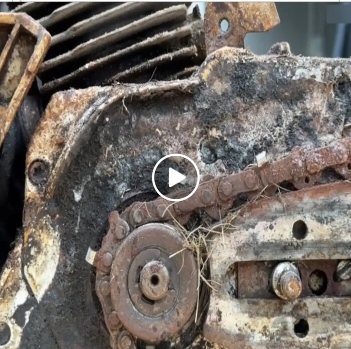 Närbild på en motorsåg med gräs lindat runt drevet där kedjan sitter. Delen verkar rostig och smutsig.
