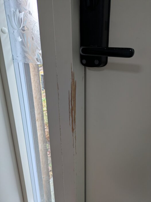 Repor på dörrkarm nära dörrhandtag orsakade av kattklor, behöver eventuell slipning och ommålning för förbättring.