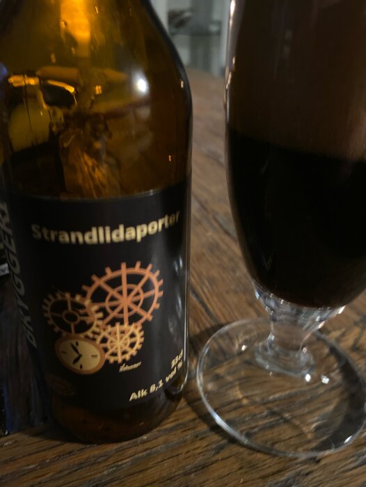 Flaska Strandlidaporter och ett glas med mörk öl på ett träbord.