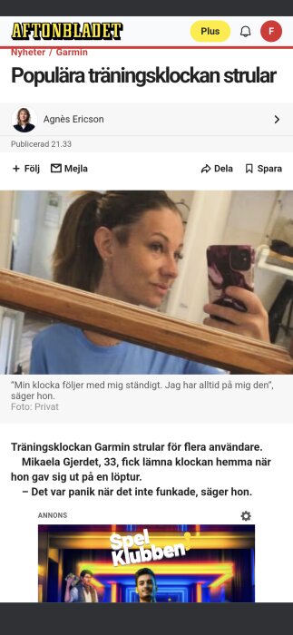 En kvinna tar en selfie i spegeln med sin mobiltelefon. Hon bär en blå tröja och har håret uppsatt i en hästsvans.