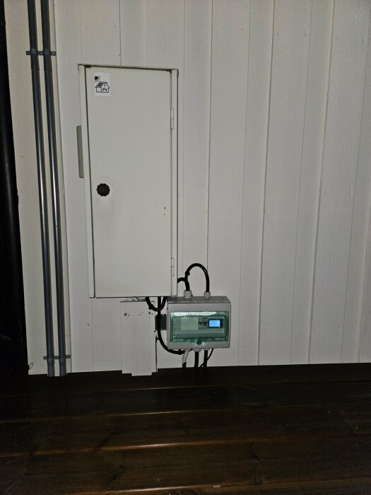 Plastkapsling för smartmätare installerad bredvid ett mätarskåp på en husfasad, med synliga kablar.