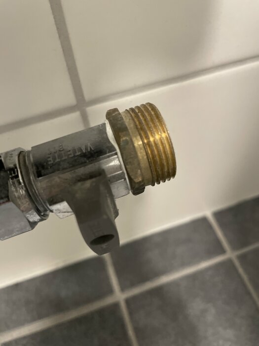 Ventil med gängor som ser ut att vara monterad med silikon, kakelvägg i bakgrunden.