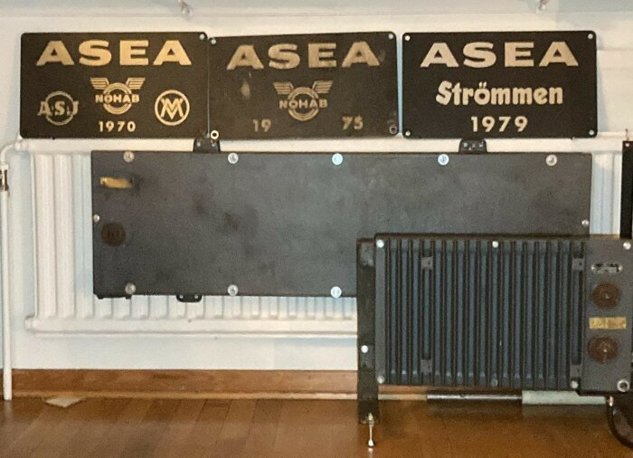 Svart kamin monterad på vägg framför radiator, skyltar märkta ASEA ovanför.