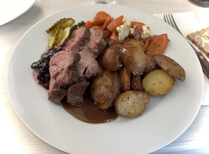 Tallrik med kalventrecote, klyftpotatis, ugnsstekta morötter, inlagd gurka, gelé och pepparsås.