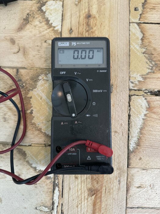 Digital multimeter Fluke 75 ligger på ett träbord, inställd på att mäta växelspänning. Den har två anslutna testkablar, en röd och en svart.