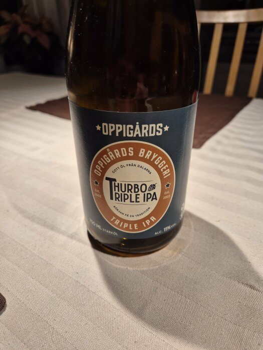 Flaska med Oppigårds Thurbo Triple IPA, 75 cl, 11% alkohol, placerad på ett bord med vit duk.