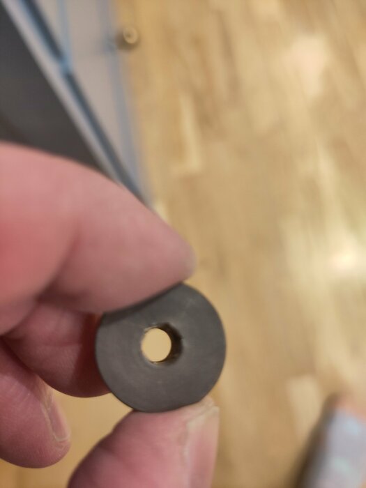 Möbelskruv med rund bricka och hål, hålls mellan fingrar, ljus träbakgrund.