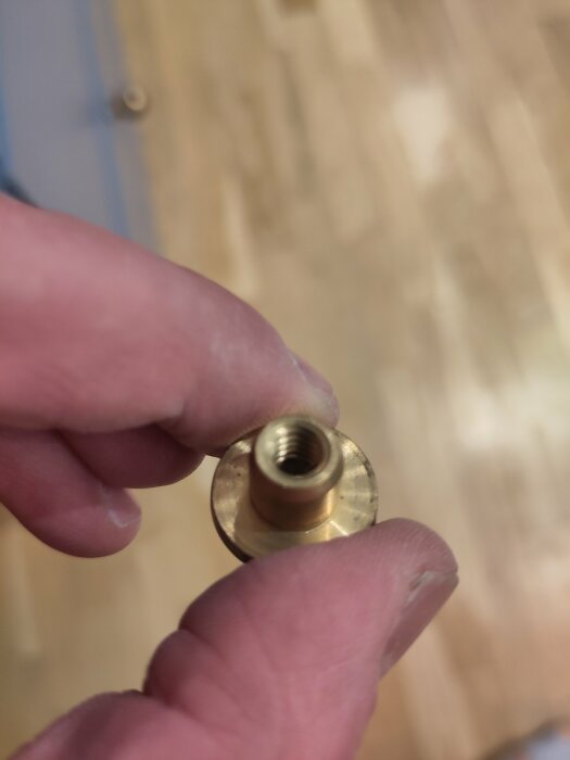 Närbild av en metallisk möbelskruv som hålls mellan två fingrar, med fokus på den gängade insidan.