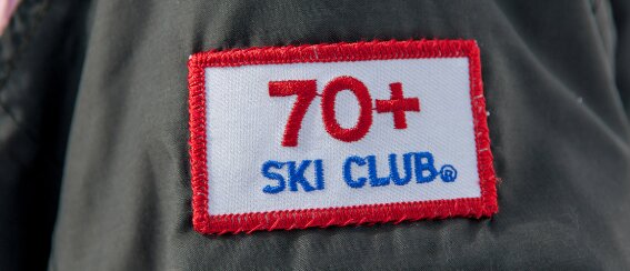 Märke med texten "70+ Ski Club" på en jacka.