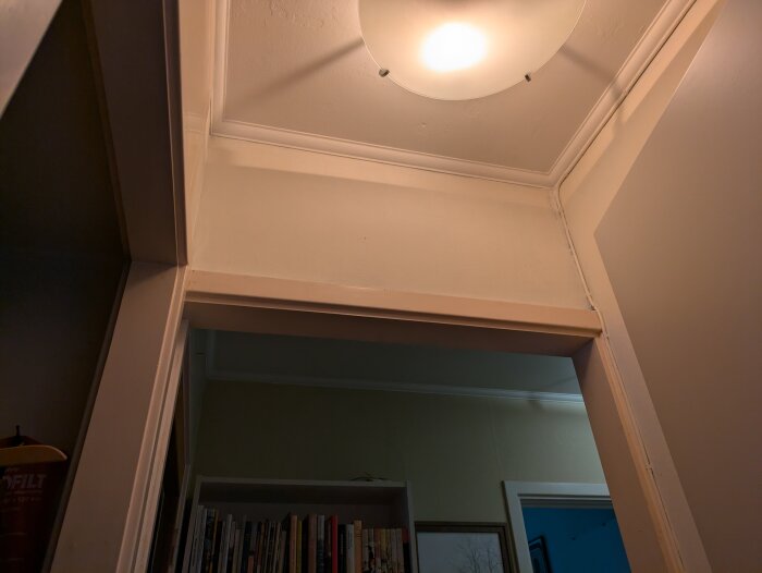 Övre del av hall i ett 60-talshus med taklampa och bokhylla i bakgrunden, visar en vägg som diskuteras för eventuell renovering.