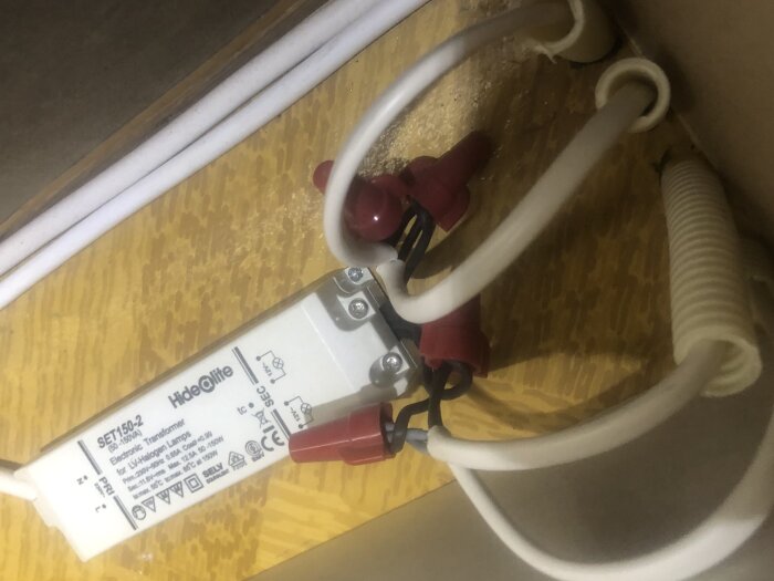 Elektronisk transformator med kablar i kabelrör på en träyta, kopplad till belysning på kattvind.