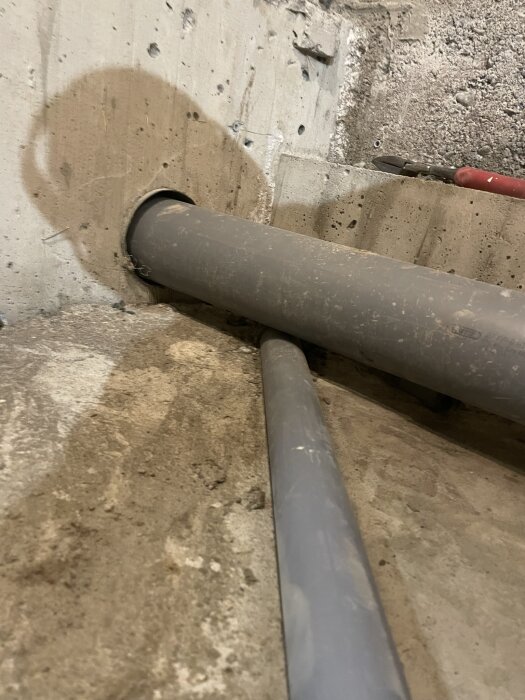 Plaströr för avlopp genom betongvägg, en del av renoveringsprojekt med dränering och avloppsrörinstallation i källare. Verktyg synliga i bakgrunden.