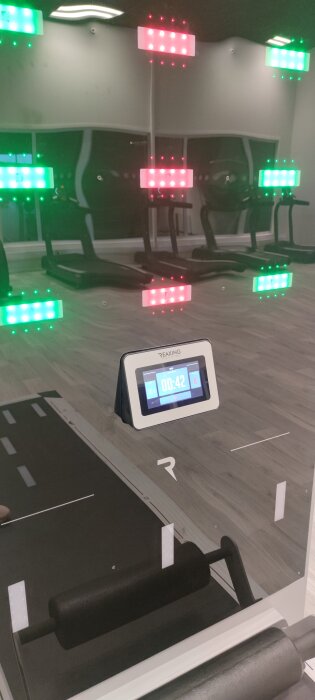 Träningsstudio med digital tidtimer och LED-belysning i olika färger. Speglar och löpband syns i bakgrunden.