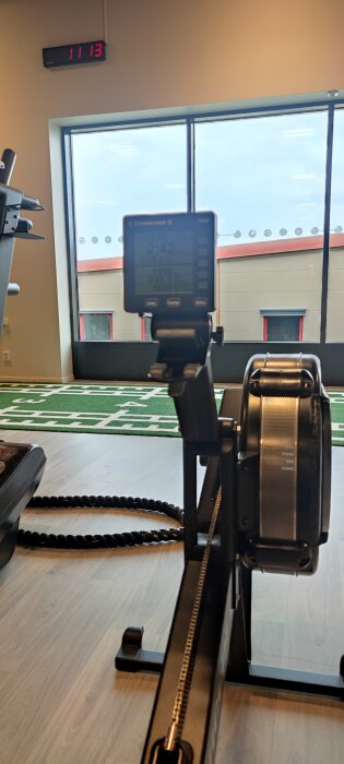 Roddmaskin i gymmet med en digital display och utsikt mot en byggnad utanför fönstret.