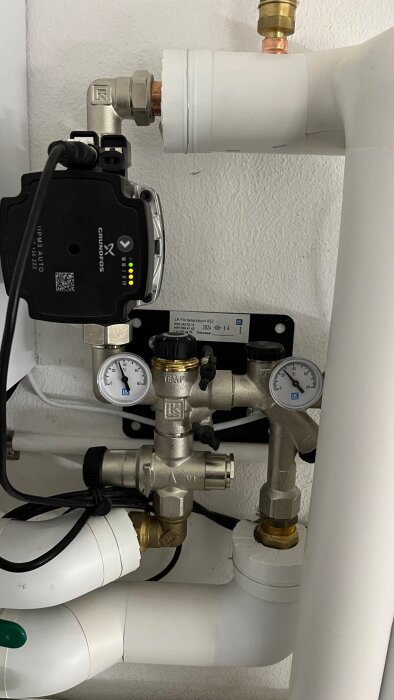 Värmeinstallation med en Grundfos pump och LK fördelarshunt, två termometrar synliga. Rörsystem i en renoverad huskällare.