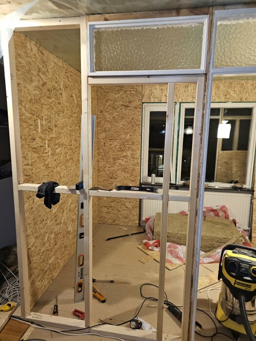 Byggarbetsplats i ett sovrum med träreglar, verktyg och isoleringsmaterial.