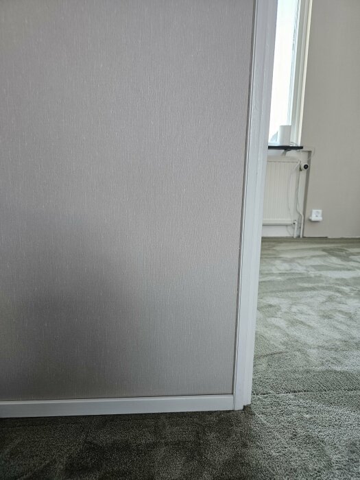 Vägg och dörrkarm i ett rum med grönaktig matta syns, del av ett sovrum under renovering.