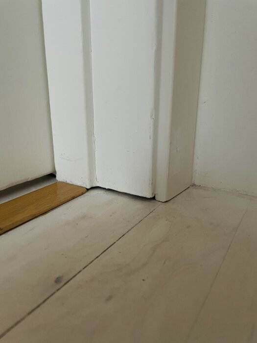 Glipa mellan golv och dörrkarm; nya vita dörrfoder med trälist syns.