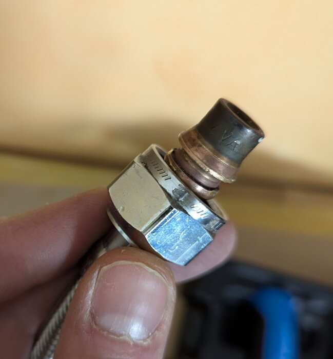 Närbild av en hand som håller en metalldel, troligen en rörkoppling med en mindre anslutning på toppen, i ett byggprojekt för blandare.