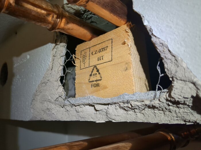 Rördragning genom ventilationstrumma med träblock och kopparrör i äldre hus, misstänkt eternitmaterial syns i närbild.