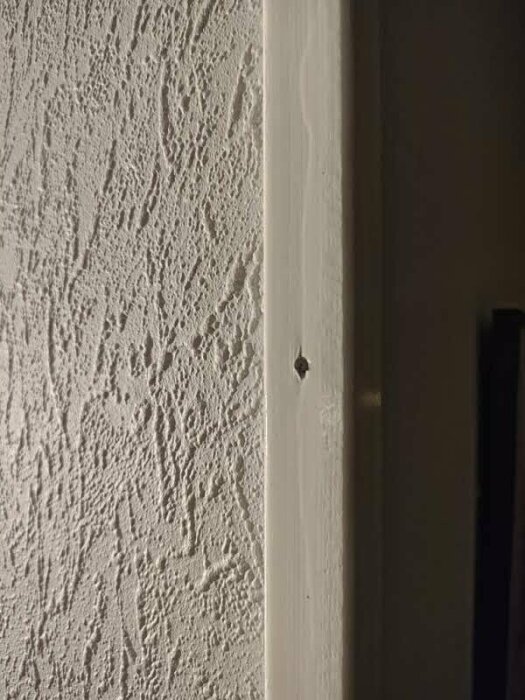 Närbild av vägglist med synligt spikhål mot en mönstrad vägg.