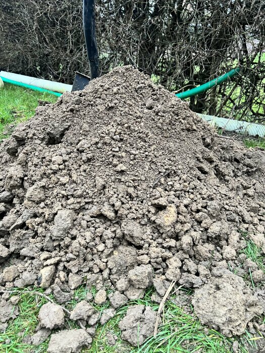 En hög jord med en spade i en trädgård, omgiven av grönska och buskar.