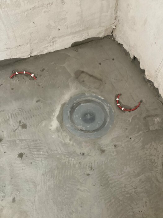 Golvyta med golvvärmeslingor som sticker upp ur flytspacklat område, omgivning i grått med en central avloppsbrunn.