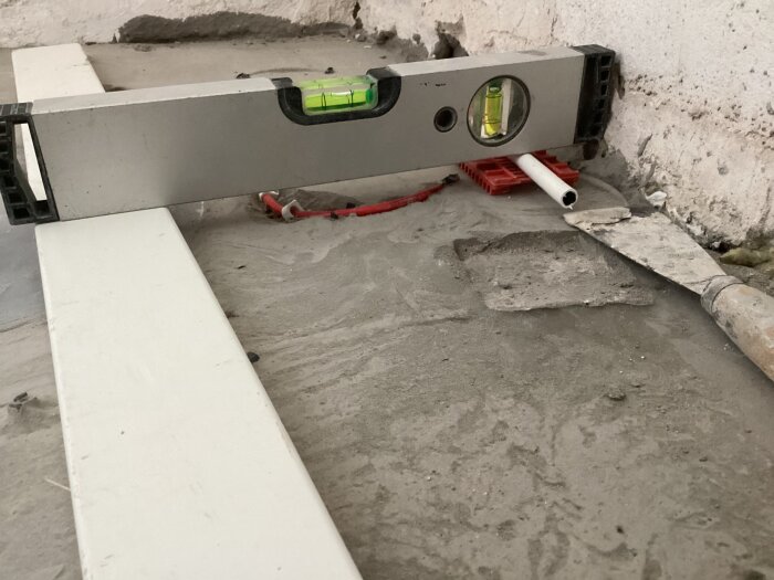 Byggnivå på flytspacklat golv med synlig golvvärmeslinga och vattenpass.