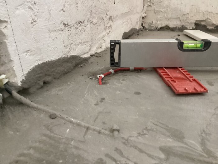 Flytspacklat golv med golvvärmeslingor och ett vattenpass på golvet, synlig röd förhöjningsring används för att mäta bygghöjd.