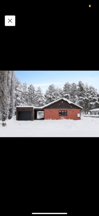 Rött tegelhus med snötäckt omgivning och angränsande garage. Skog i bakgrunden.