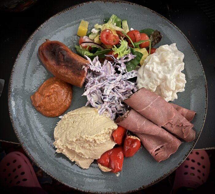 Tallrik med bratwurst, rostbiff, potatissallad, coleslaw, hummus, sallad, chili/tomatröra och ostfyllda chilis.