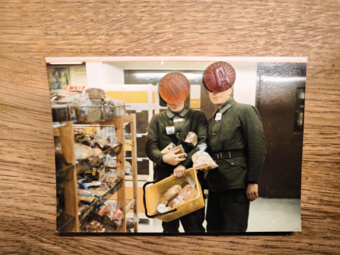 Två personer i uniformer handlar bröd och korv i en butik, håller i en korg med matvaror.