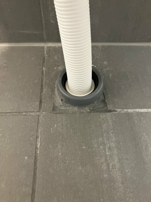 Tile cut around a white pipe with rough grouting in a bathroom, highlighting uneven tile placement and mismatched grout.