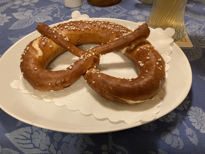 En saltad pretzel på en vit tallrik med en blå duk i bakgrunden.