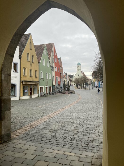 Valv med utsikt över en gata med färgglada hus och en kyrka i bakgrunden. Kullerstenstäckt väg och få människor syns.