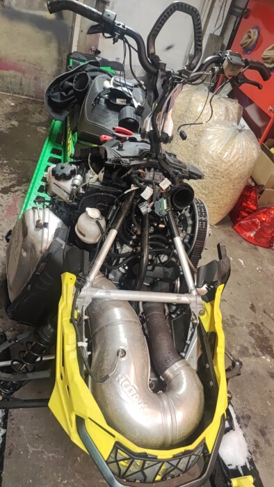 Snöskoter med öppet motorutrymme, synliga delar och verktyg, möjligtvis för felsökning eller rengöring av rave portarna.