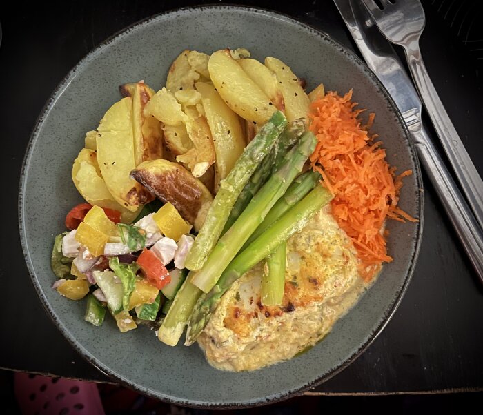 Tallrik med torsk i krämig sås, klyftpotatis, kokt sparris, rivna morötter och sallad med grönsaker och ost.
