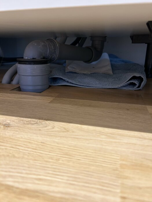 Ett avloppsrör under en diskbänk med en handduk under för att fånga upp läckage.