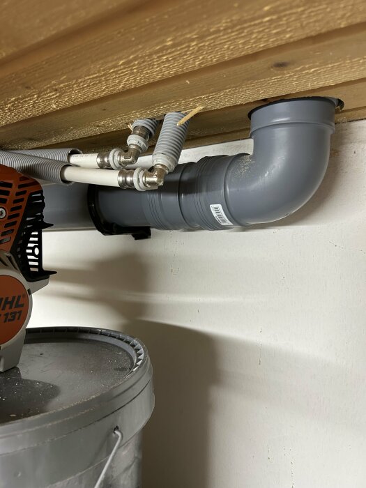 VVS-installation med rör och kopplingar under ett trätak, verktyg på en plasthink.