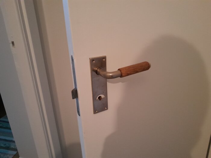Trähandtag på dörr med vit yta och metallplatta.