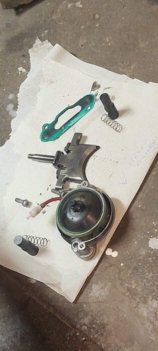 Isärplockade delar av en motor eller maskinkomponenter på ett papper, inklusive fjädrar och tätningar, ligger på ett verkstadsgolv.