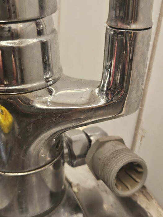 Förgrening på vattenkran med fäste för anslutning, belägen direkt på kranen, med reflekterande metallfinish mot kaklad bakgrund.