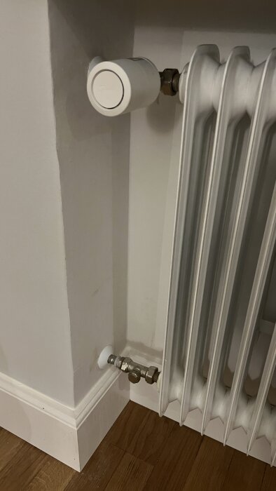 Radiator med Danfoss Ally termostat på Danfoss RA ventil, golv med träpanel.