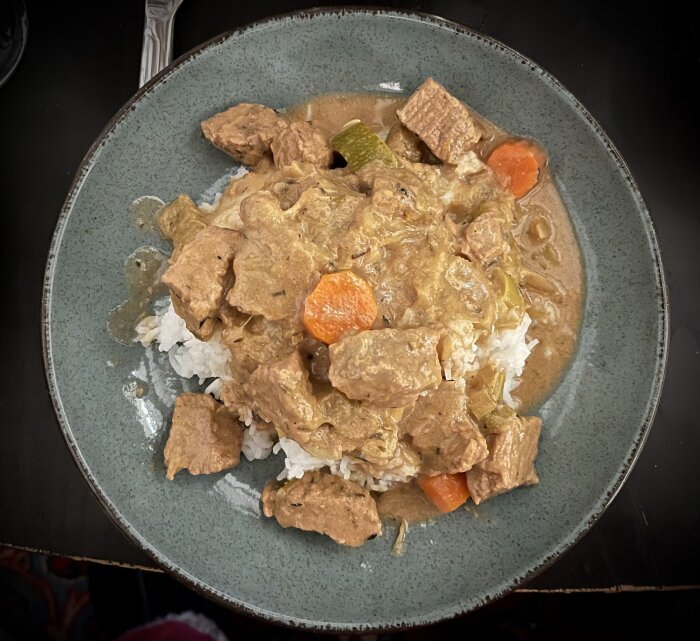 Höstgryta serverad med ris, innehållande bitar av kött, morot, vitkål och squash, på en tallrik.