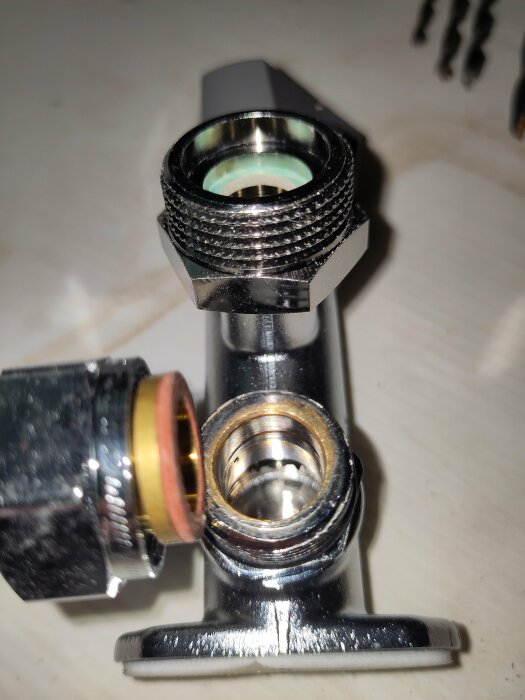 Närbild av en Vatette tappventil med synliga gängor och kopplingsdelar, inklusive nippel och klämhylsa, på ett lyst metallunderlag.