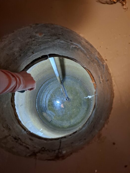 Hål i betongplatta under skafferigolv, fylld med vatten cirka 30 cm djupt, sett uppifrån.