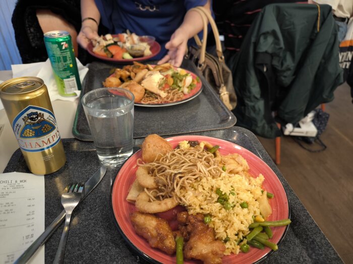 TvÄ tallrikar med asiatisk buffé, en burk Champis och ett glas vatten.